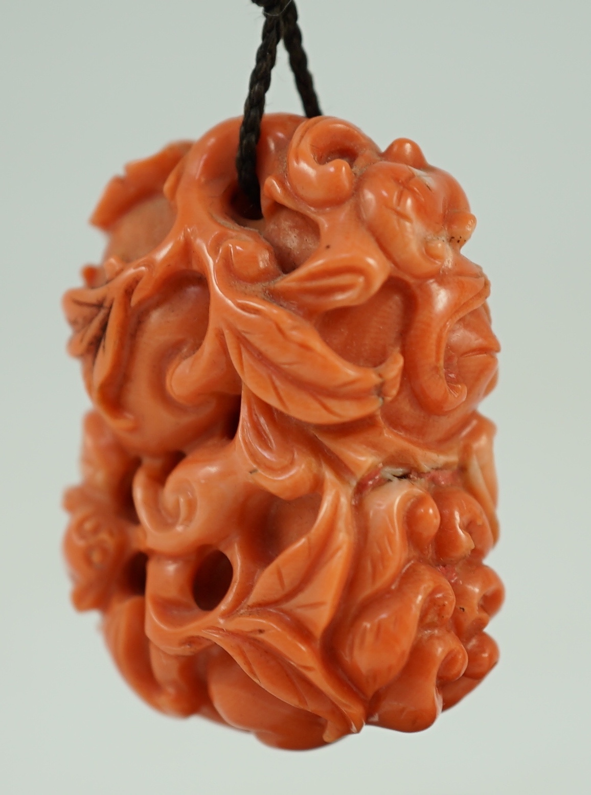 A good Chinese coral ‘fruit and bats’ pendant, 19th century, 3.7cm, later suspension stand